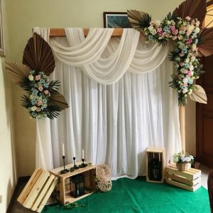 Backdrop dekorasi pernikahan rustic bohemian kain putih draping bunga daun palem lilin kotak kayu